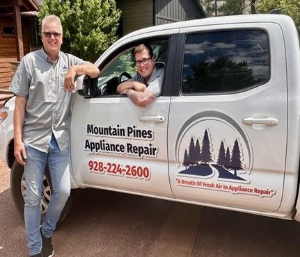Two people beside a white Mountain Pines Appliance Repair truck with company logo and phone number.