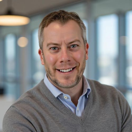 A man in a grey sweater and blue shirt is smiling for the camera.