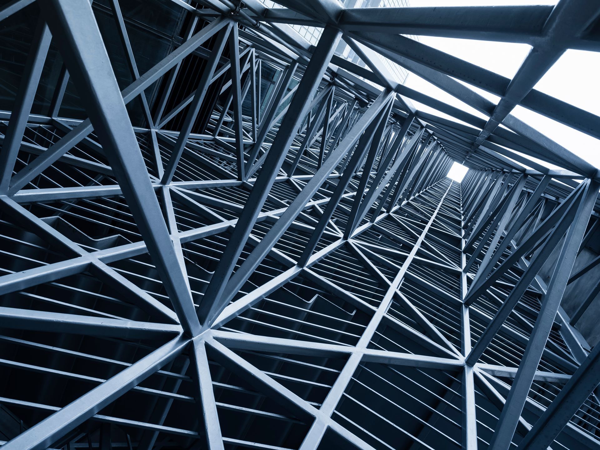 Steel structure of a tall building, viewed from below, angled lines converging toward a square opening at the top.
