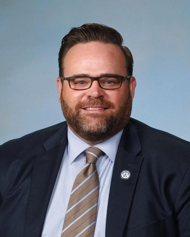 A man with a beard and glasses is wearing a suit and tie.