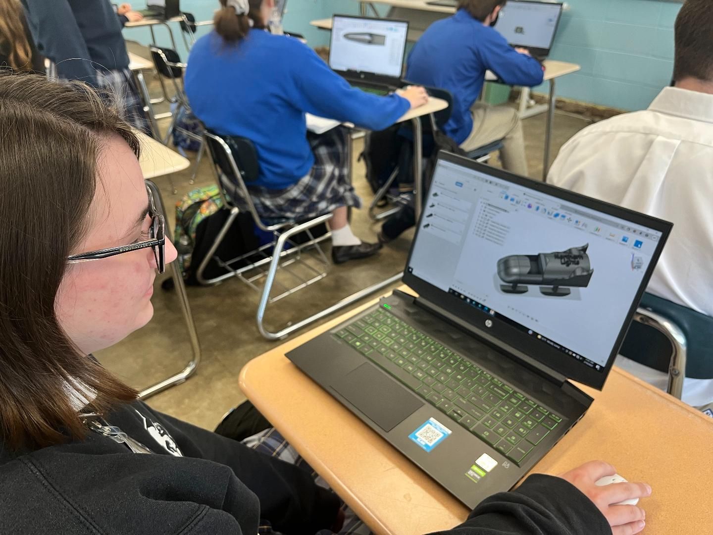 A girl is sitting at a desk looking at a laptop computer.