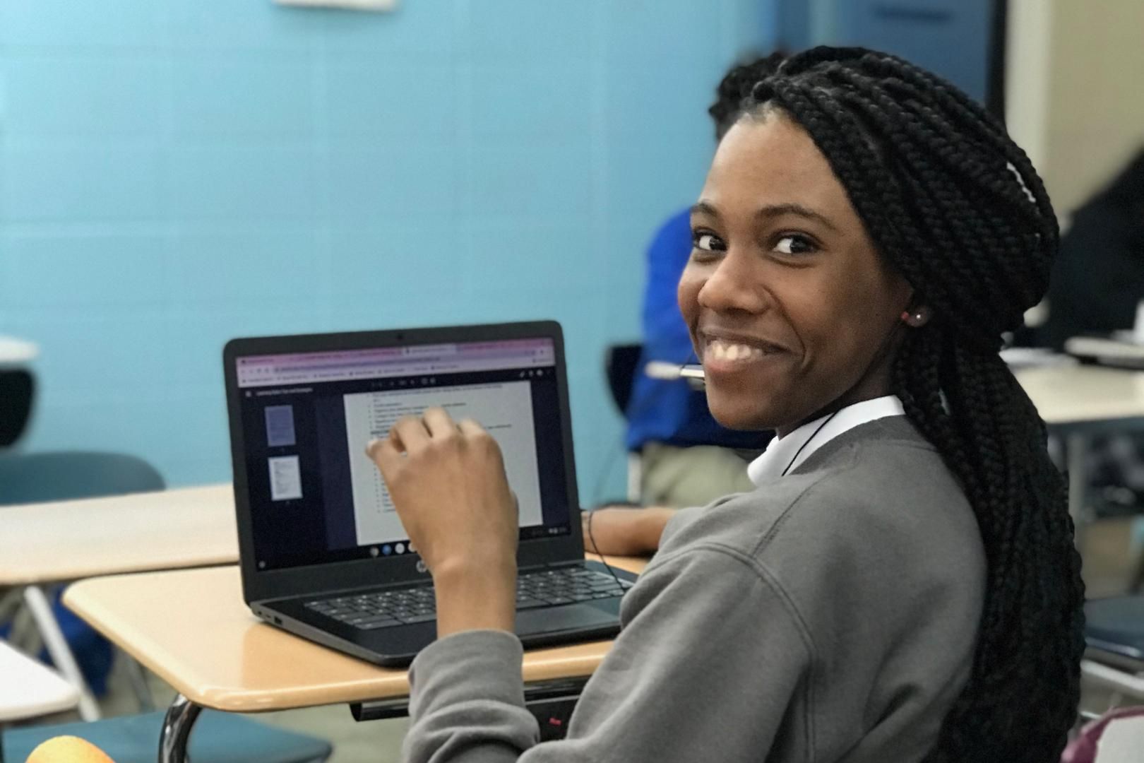 A woman is sitting at a desk with a laptop and smiling.