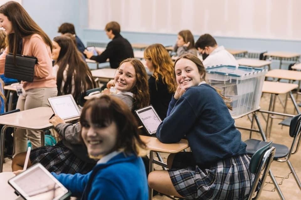 A group of students are sitting at desks in a classroom using laptops.