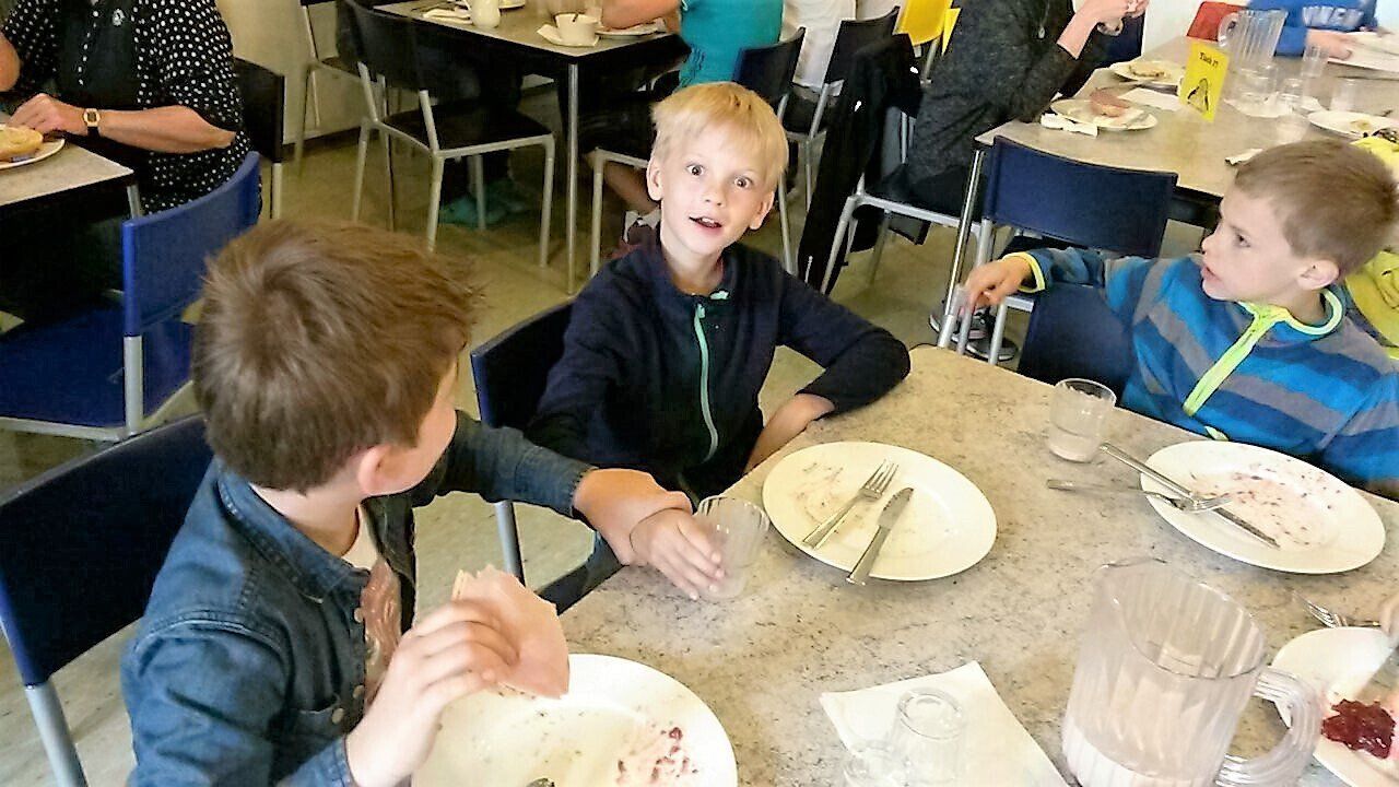 Eine Gruppe Kinder sitzt mit Tellern voller Essen an einem Tisch.