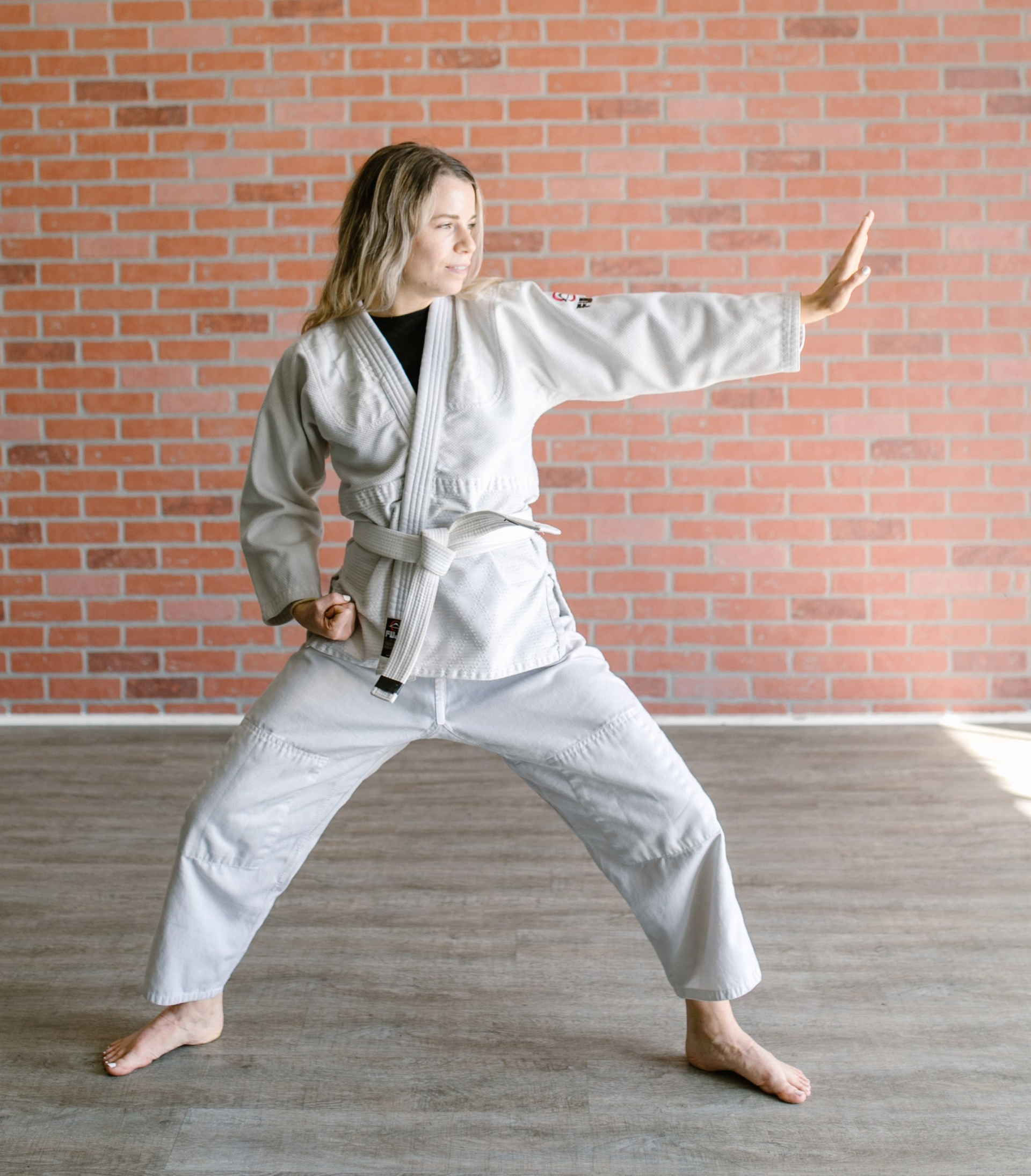 Eine Frau in einer Karateuniform übt Karate vor einer Backsteinmauer.