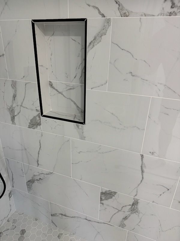 White marble-pattern shower wall with a recessed rectangular niche and a black trim frame.