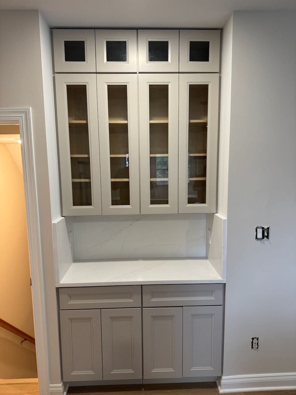 Built-in white kitchen cabinet with glass doors, countertop, and lower storage drawers in a hallway niche