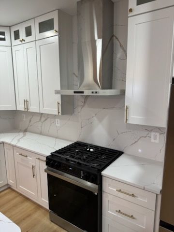 Bright white kitchen with gas stove, stainless range hood, cabinets, and light wood floor.