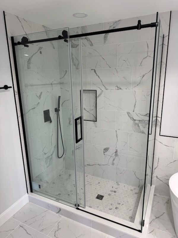 Glass shower with black hardware and white marble tile in a bathroom
