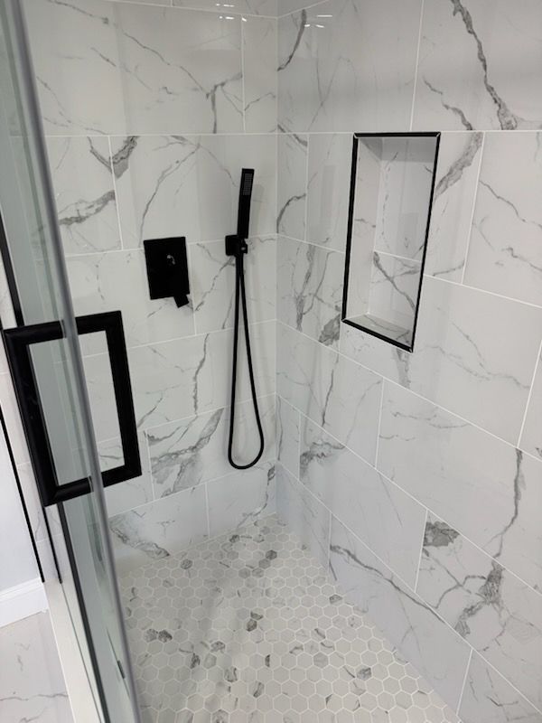 Modern shower stall with white marble-pattern tile, black fixtures, and glass door.