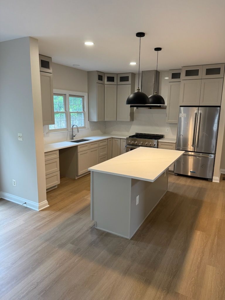 Modern kitchen with white cabinets, stainless fridge, center island, and wood floors