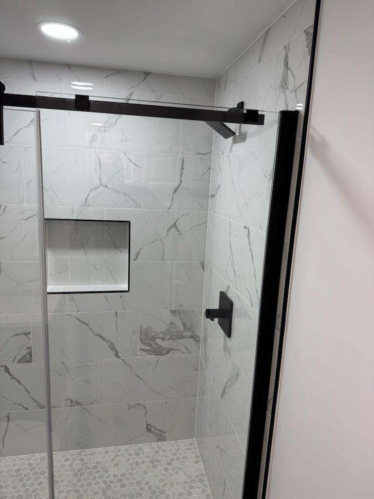 Modern tiled walk-in shower with black hardware, glass door, and recessed niche cabinet.