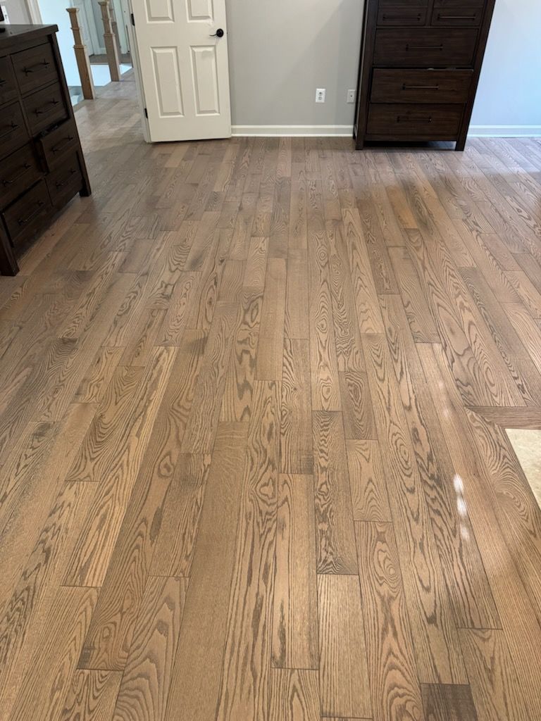 Empty bedroom with light wood flooring, open white door, and dark wood dressers on both sides.