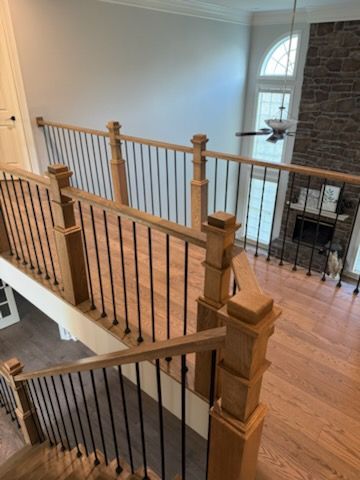 Interior staircase with wooden railing, black balusters, and a stone fireplace in the background