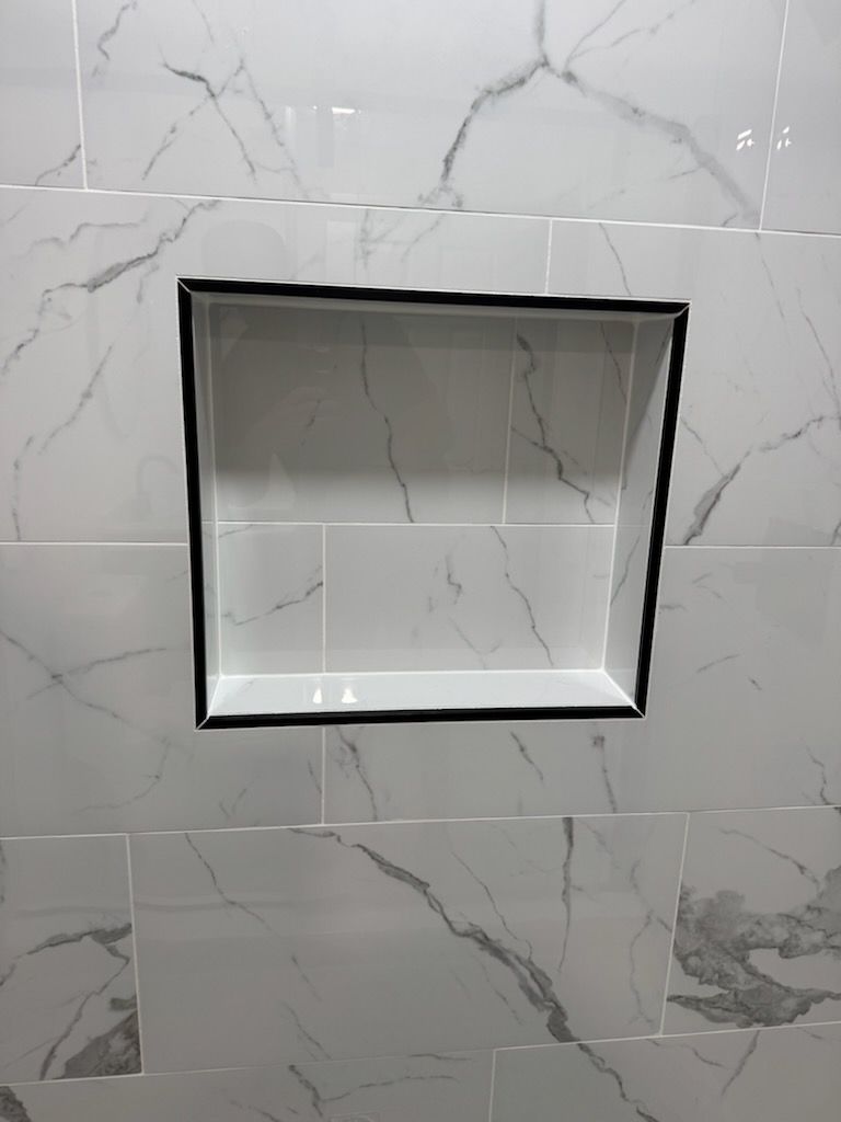 White marble-tiled wall with a square recessed niche outlined in black.