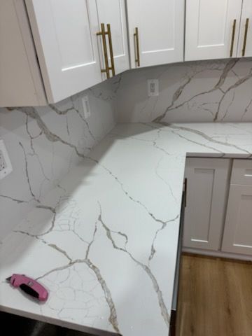 White kitchen countertop with marble-look backsplash and gold cabinet pulls, with a pink tape measure on the counter