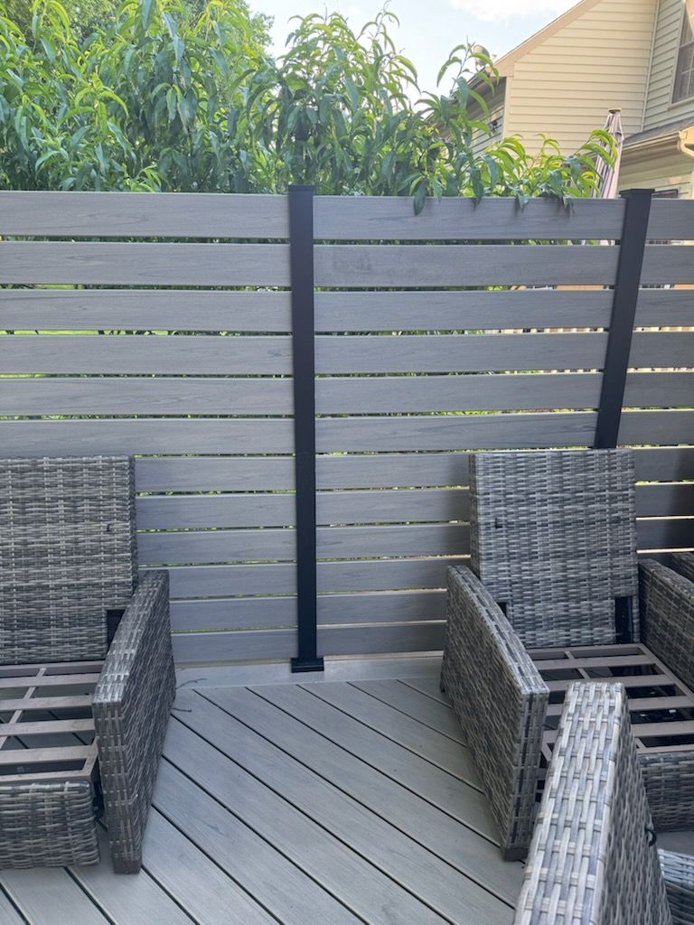 Patio seating area with woven chairs on a gray deck beside a horizontal slat fence and greenery