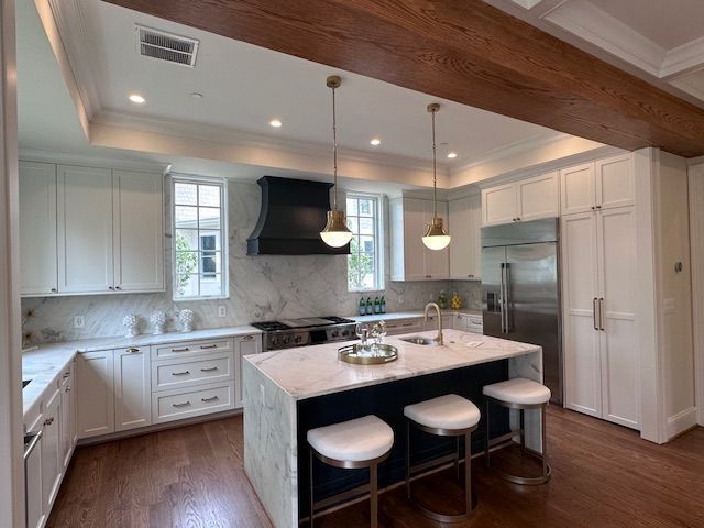 Bright modern kitchen with white cabinets, marble island, black range hood, and three stools