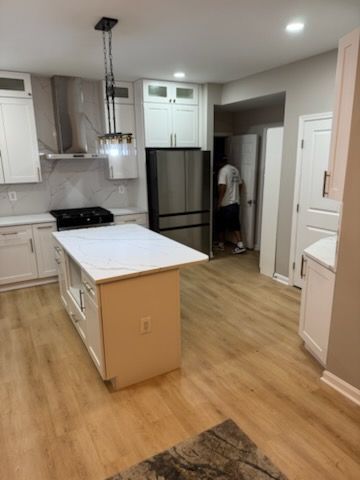 Modern kitchen with white cabinets, stainless fridge, and a central island on light wood flooring