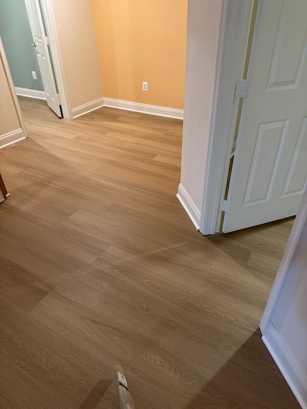 Empty hallway with light wood flooring, beige walls, white trim, and open doors.