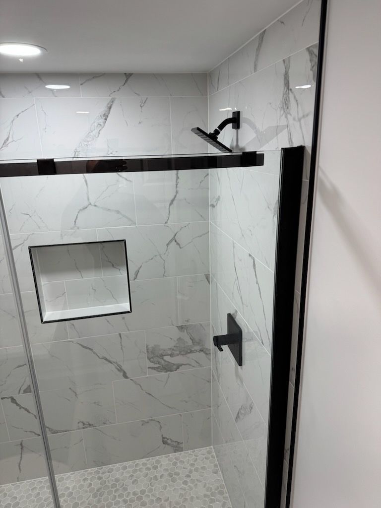Modern shower stall with white marble tile, black trim, built-in shelf, and glass door handle