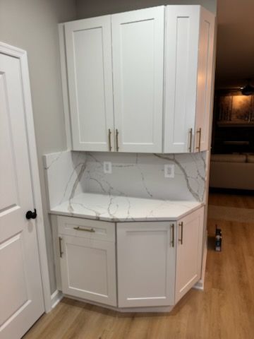White kitchen corner cabinet with marble-look countertop and backsplash in a bright room