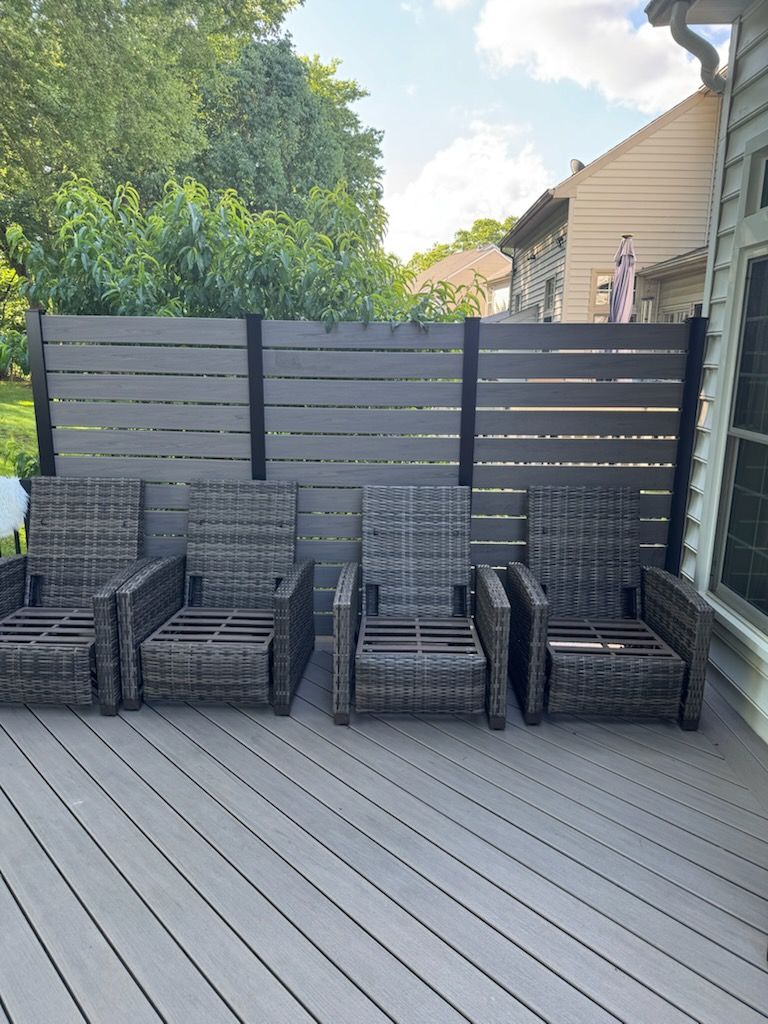 Backyard deck with four gray wicker chairs lined against a privacy fence