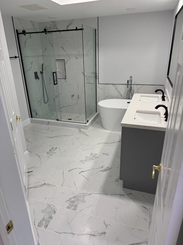 Modern bathroom with glass shower, white marble tile, and dark vanity.