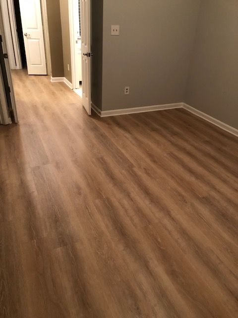 Empty apartment hallway with wood-look flooring and gray walls, doors open on the left.