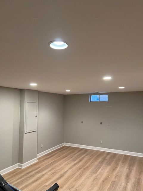Empty finished basement room with gray walls, wood-look floor, recessed lights, and a small high window