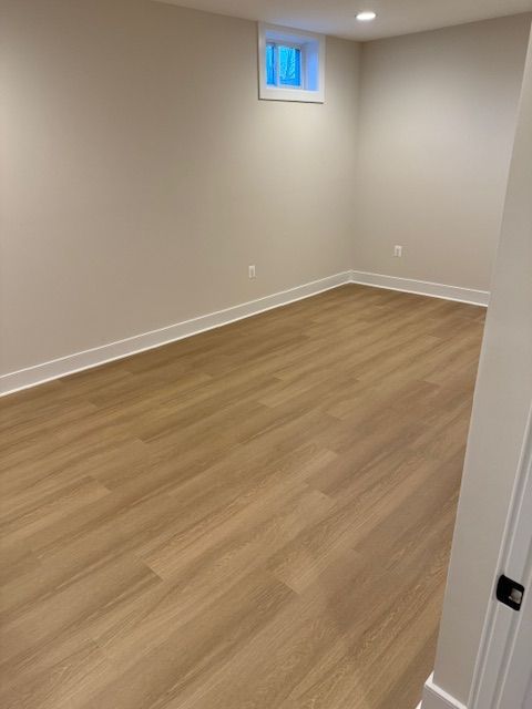Empty beige room with wood flooring, a small high window, and white trim.