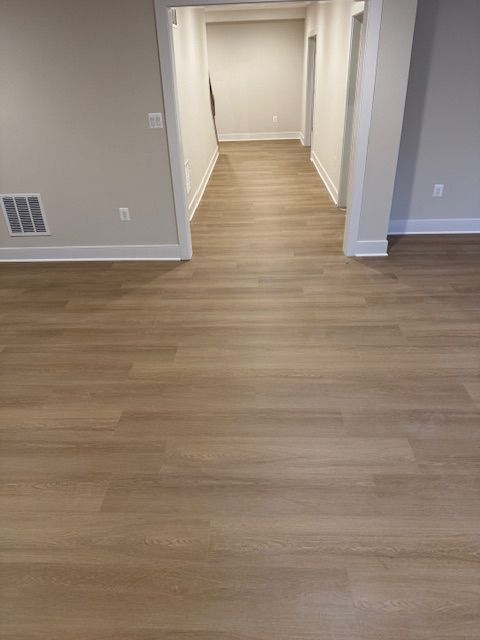 Empty hallway with light wood flooring, white walls, and an open doorway in the center.