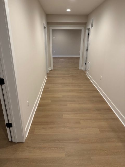 Empty beige hallway with wood flooring, white walls, and doorways on both sides
