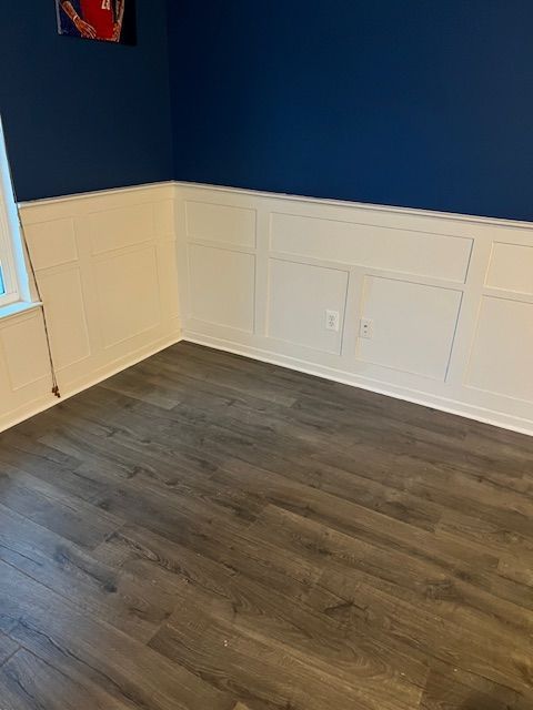 Empty room with blue walls, white wainscoting, and dark wood flooring
