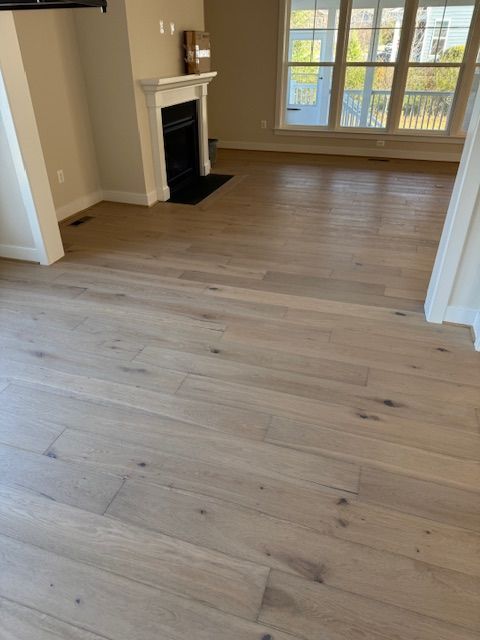 Empty beige living room with light wood floors, fireplace, and large windows