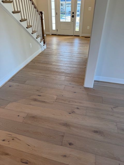 Empty foyer with light wood floors, white walls, staircase, and front double doors.