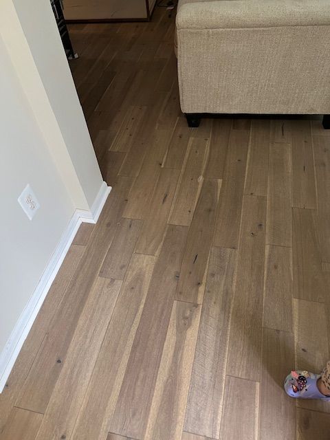 Wood-look floor in a hallway with a beige sofa at right and a child’s shoe in the corner.