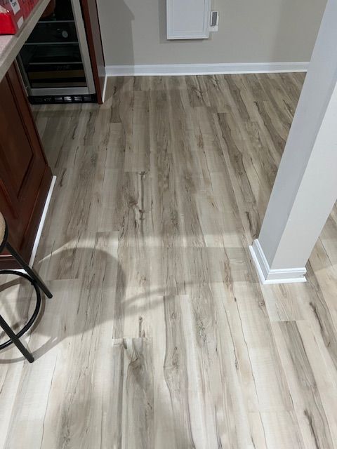 Light wood flooring in a hallway with a white column, baseboards, and a cabinet at left.