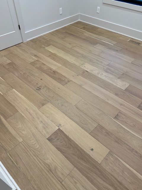 Empty room corner with light wood flooring and white baseboards