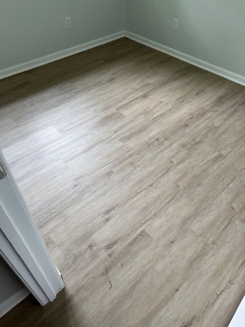 Empty room corner with light wood flooring and pale green walls