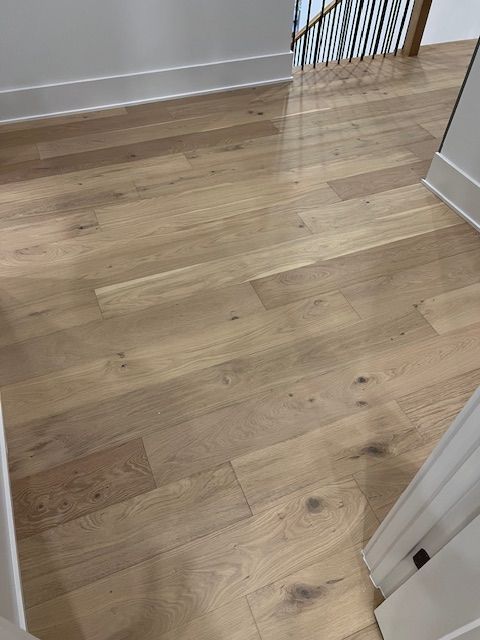 Wooden hallway floor with light oak planks and white door frames leading to a stair railing.