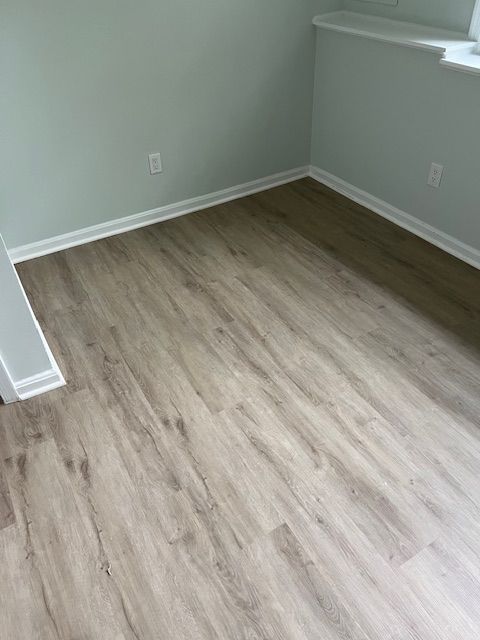 Empty room with light gray walls, wood-look flooring, and white trim near a window.