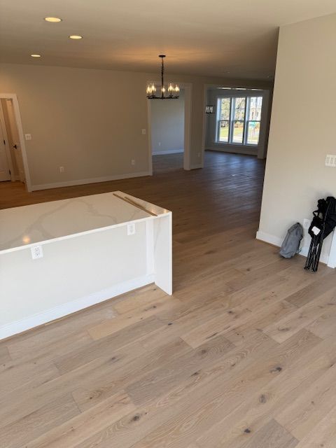Empty open-plan living room with light wood floors, gray walls, and a chandelier near the dining area.