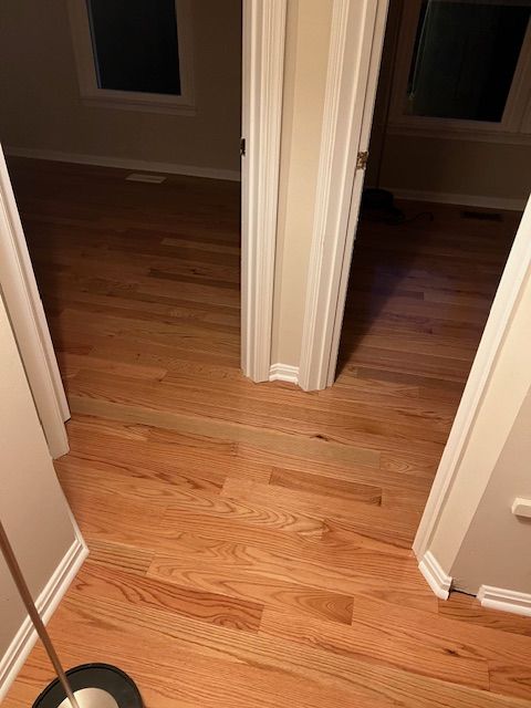 Hallway with hardwood floors and open doorways into two dark rooms