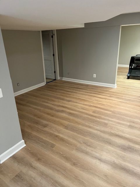 Empty gray room with light wood flooring and a doorway leading to another room