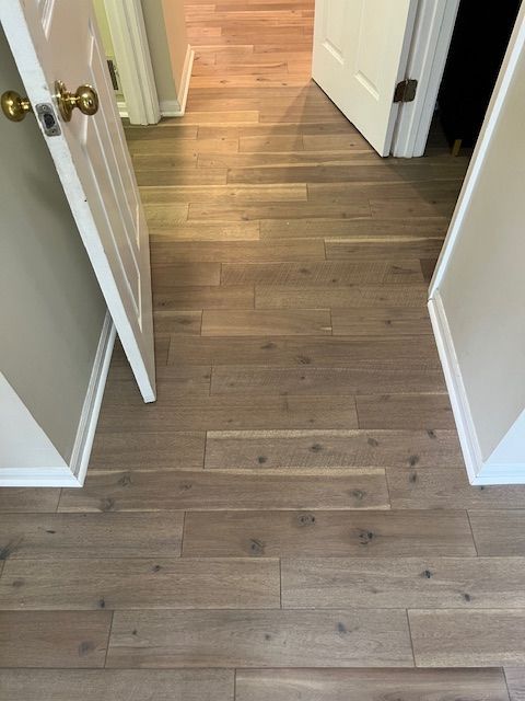 Hallway with wood plank flooring and open white doors leading to a brighter room