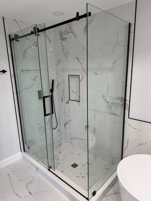 Modern glass walk-in shower with marble-look tile, black hardware, and white bathroom floor