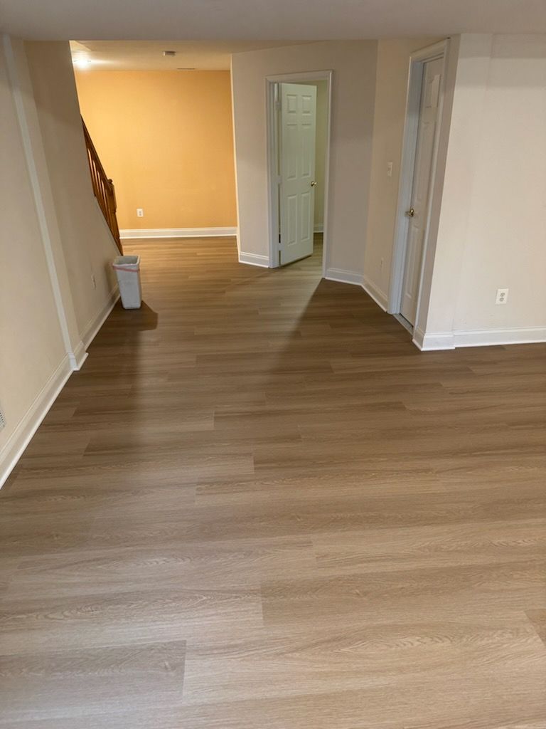 Empty hallway with wood-look flooring, beige walls, and an open door at the end.