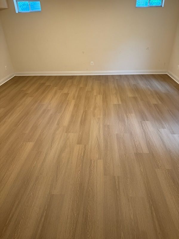 Empty room with light wood flooring, beige walls, and two small windows.