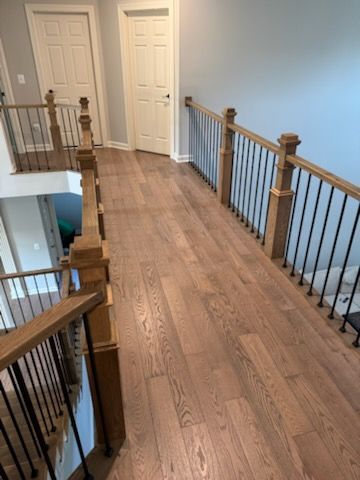 Wooden upstairs hallway with railings, white doors, and a staircase opening on the left.